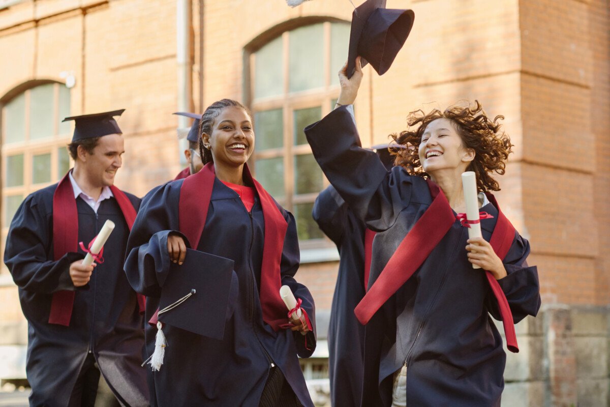 Happy graduated students in robes running along the campus outdoors