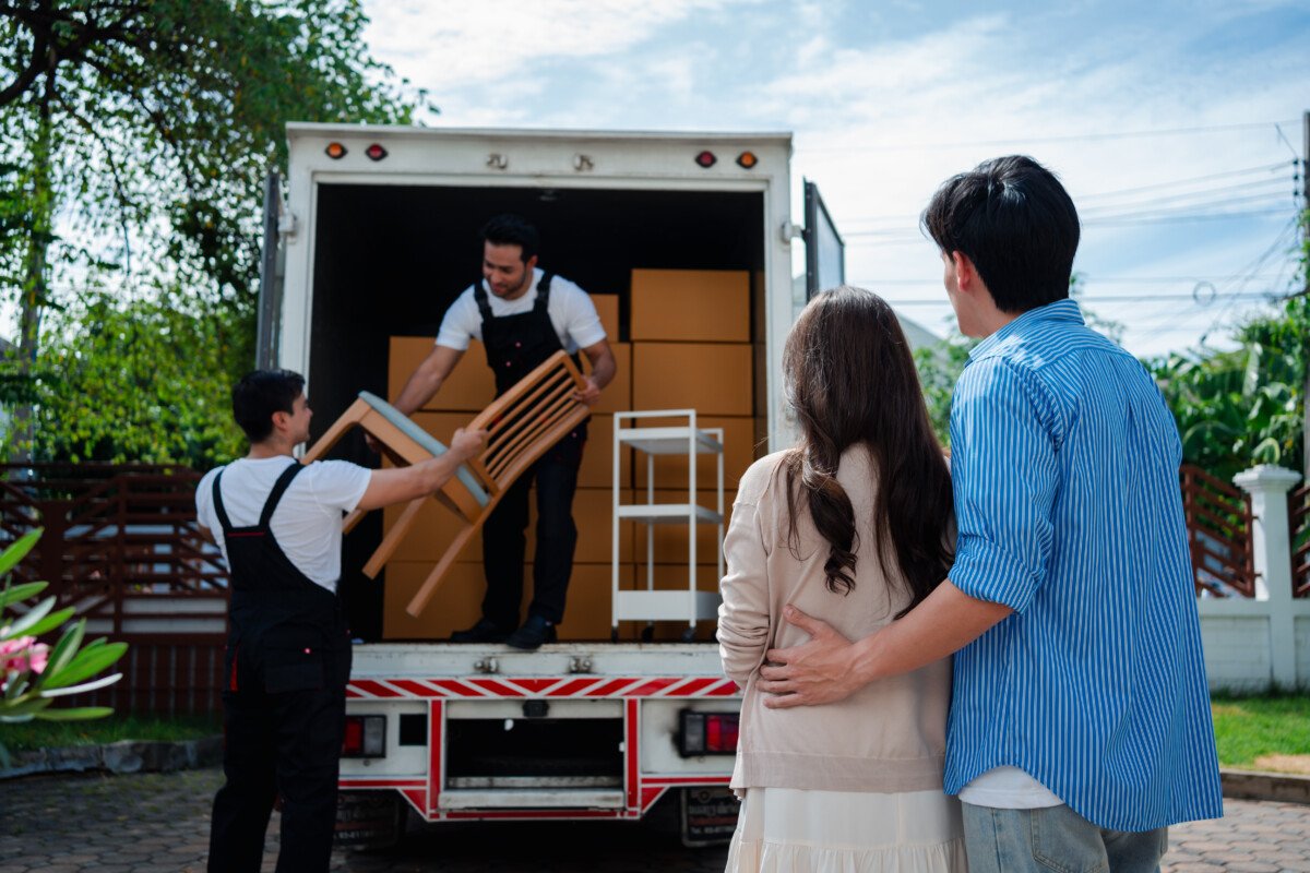Asian Couple check while unloading boxes and furniture from a pickup truck to a new house with service cargo two men movers…