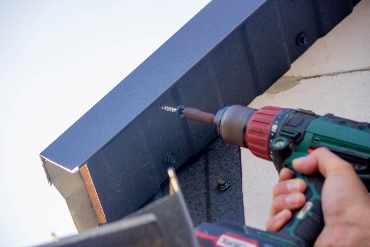 a man repairs the roof, tightens the self-tapping screw with a screwdriver. Selective focus