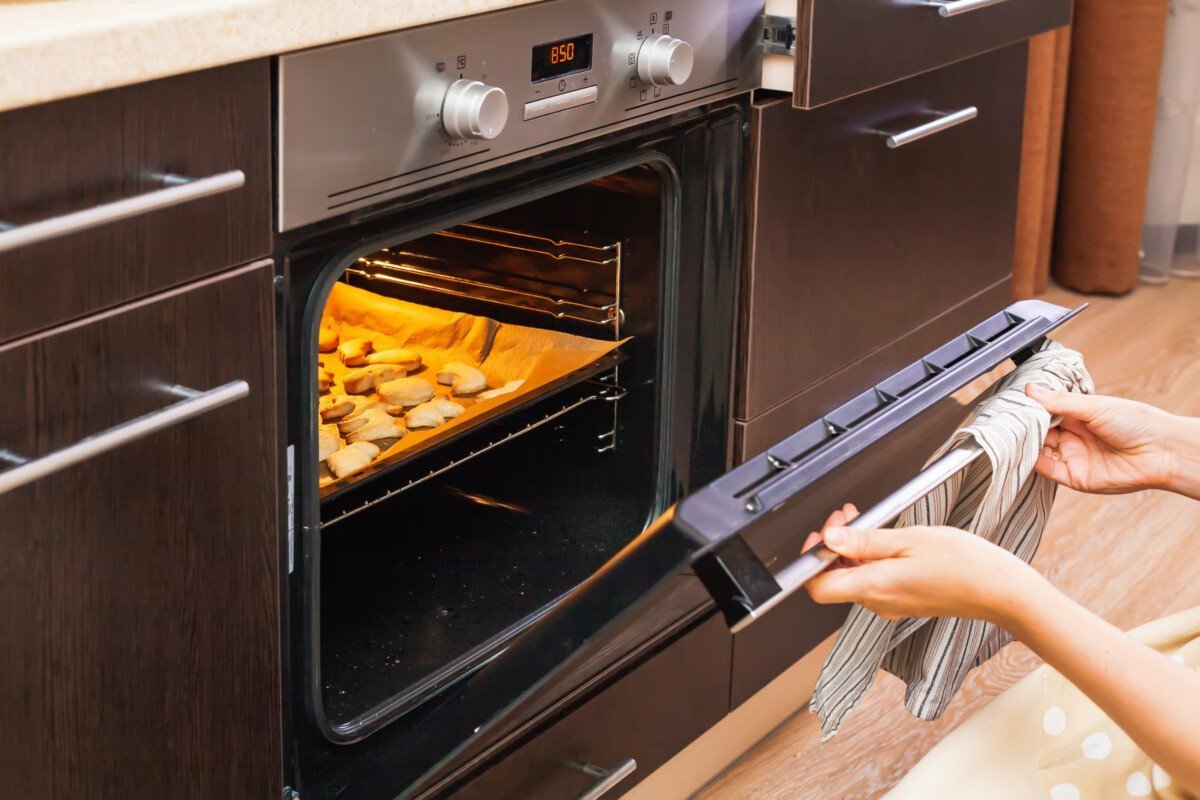 Woman opens the oven where cookies are baked for Halloween.