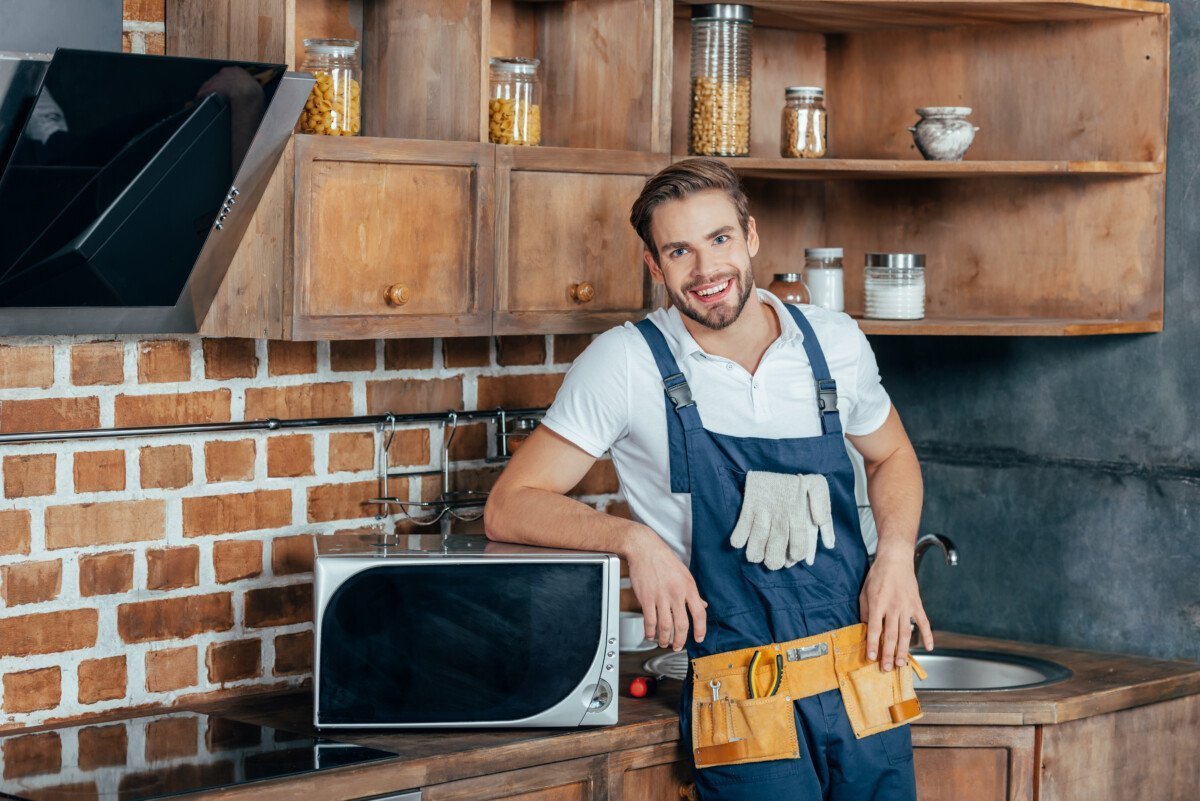 handsome young handyman leaning at microwave oven and smiling at camera