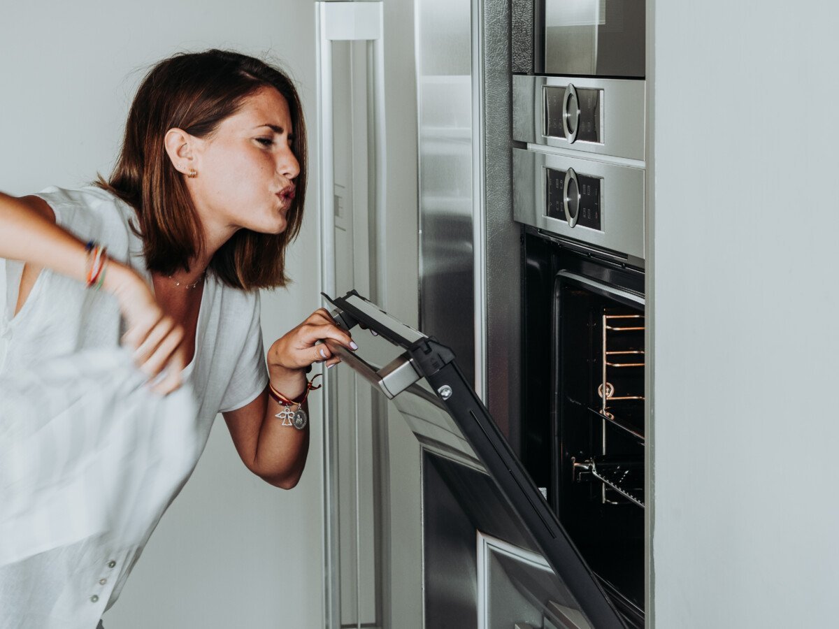 Blonde woman with green eyes in modern kitchen checks the oven because her food is burning