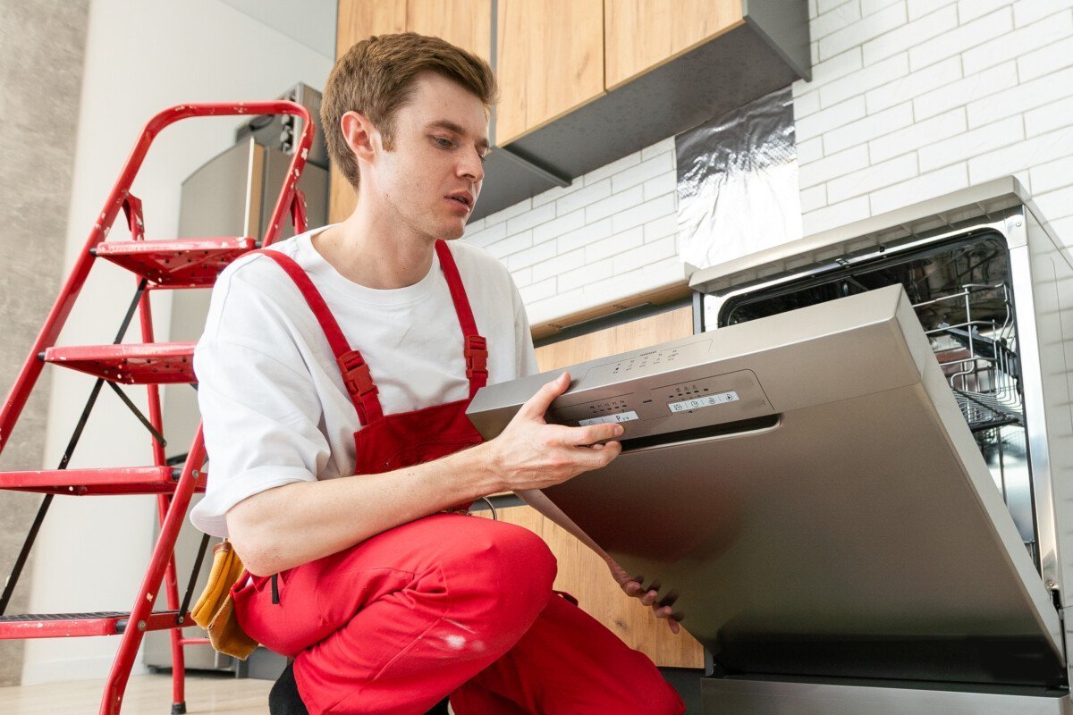Repairman checks operating state of dishwasher in kitchen.