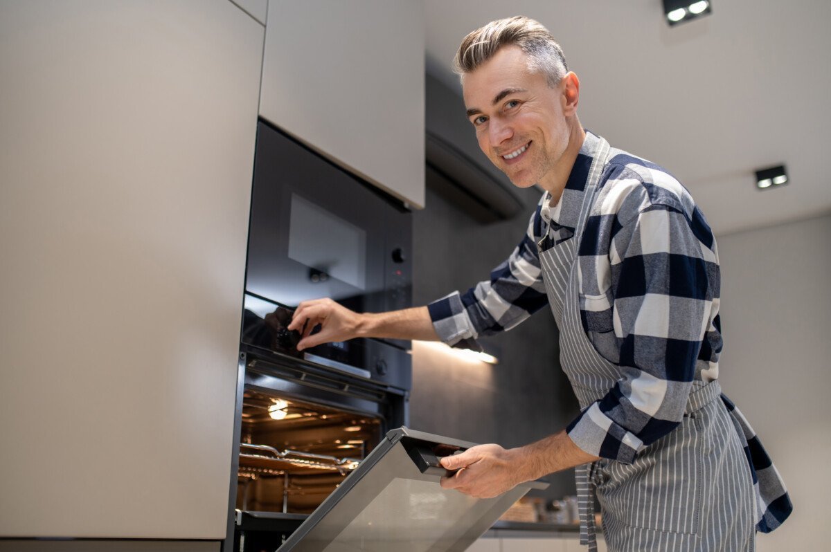 Temperature regulation. Confident smiling middle-aged man in plaid shirt and striped apron turning toggle switch to adjust…