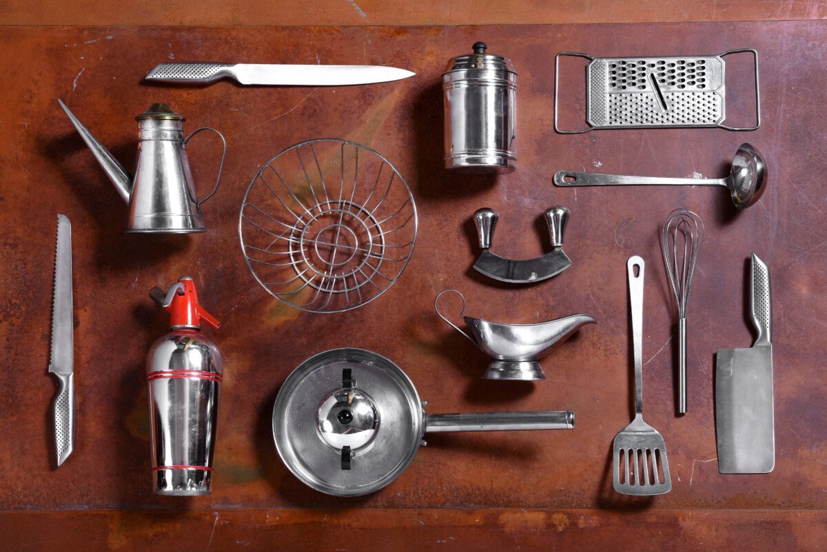 Collection of various metal kitchen utensils with a cleaver, martini shaker, pan, knives, sauce boat, wire basket,…