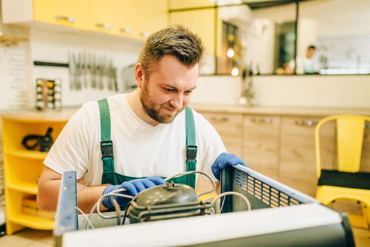 Worker in uniform repairs refrigerator compressor at home. Repairing of fridge occupation, professional service