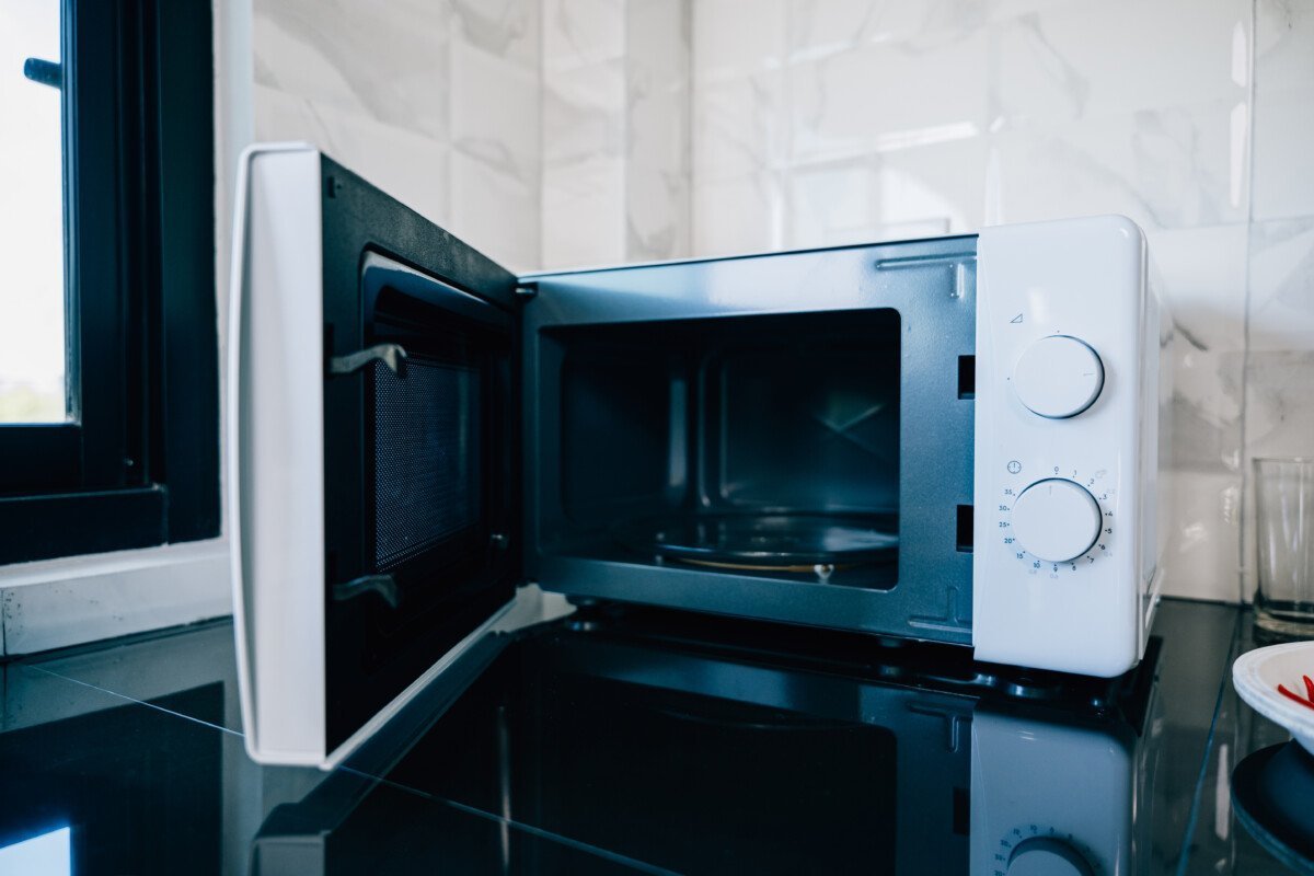 An open microwave oven door on a sleek kitchen tabletop presenting modern technology and design in household appliances.…