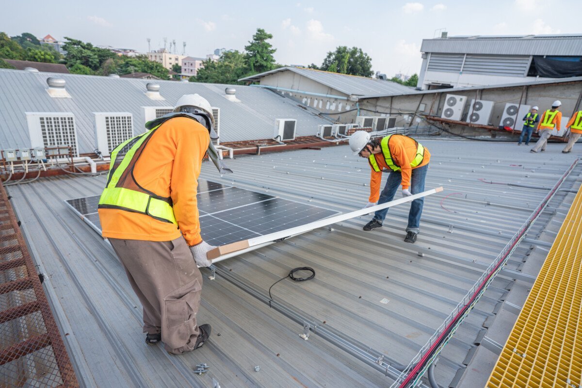 Team technicians carrying photovoltaic solar moduls on roof of factory on the morning. Installing a Solar Cell on a Roof.…