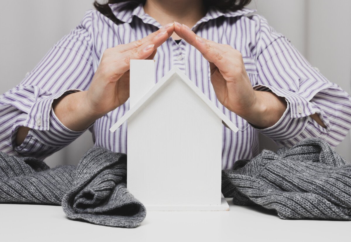 female hands folded to each other over a wooden miniature model house on a white background. Real estate insurance concept,…