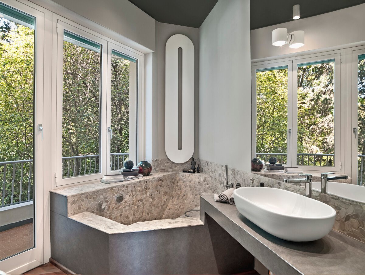 Interior view of a modern bathroom in the foreground the washbasin on the masonry top and in the corner on the background…