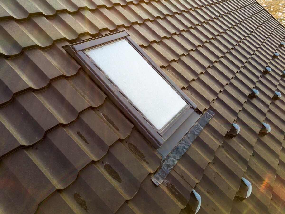 Close-up of new attic plastic window installed in shingled house roof. Professionally done building and construction work,…