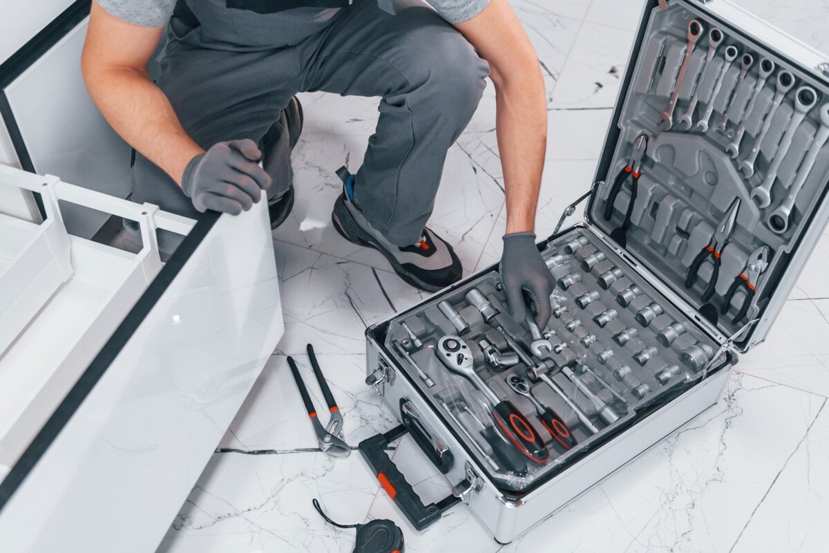 Young professional plumber in grey uniform using equipment on the kitchen and preparing for the work.